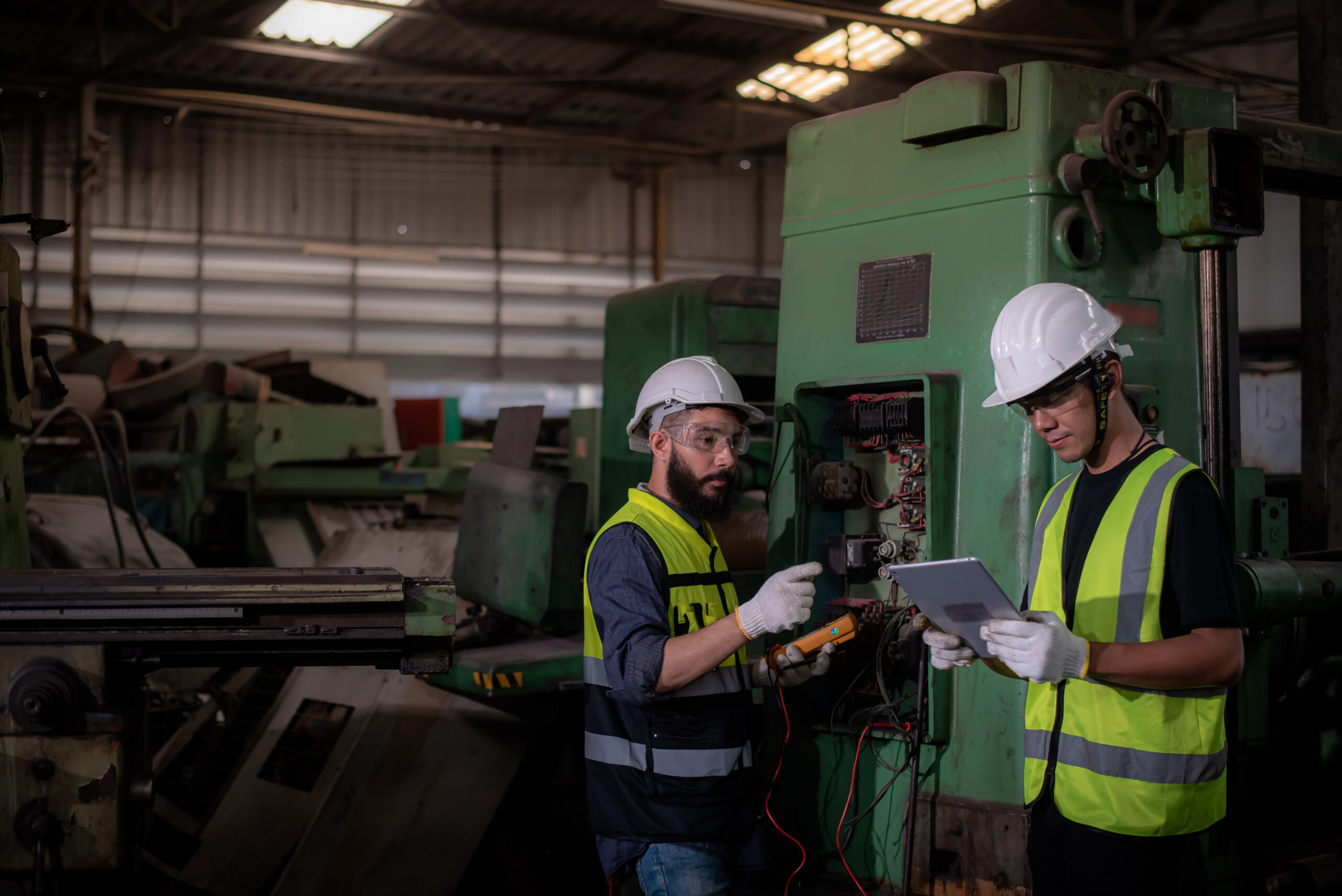 electrician latin mixed race and asian engineer in safety uniforms inspecting and maintaining the machine's electrical control cabinet in heavy industrial manufacturer factory.